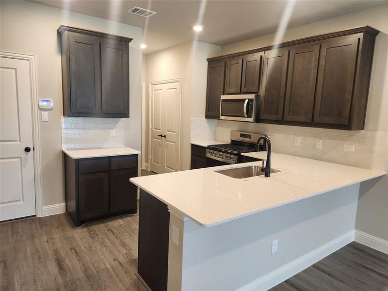 Kitchen with hardwood / wood-style flooring, tasteful backsplash, sink, appliances with stainless steel finishes, and kitchen peninsula