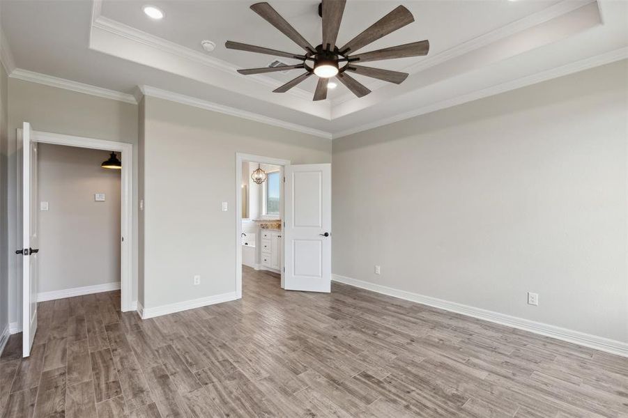 Unfurnished bedroom with ceiling fan, light wood-type flooring, a tray ceiling, and crown molding