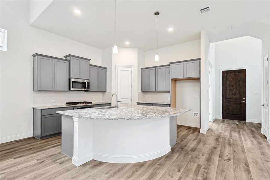 Kitchen featuring gray cabinets, sink, light wood-type flooring, and an island with sink