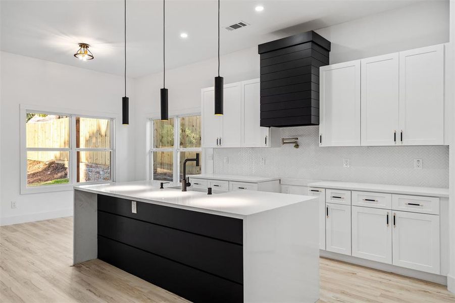 Kitchen featuring decorative light fixtures, white cabinets, a kitchen island with sink, and light hardwood / wood-style flooring