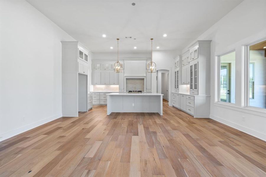 Kitchen featuring decorative light fixtures, light wood-type flooring, white cabinetry, and a kitchen island