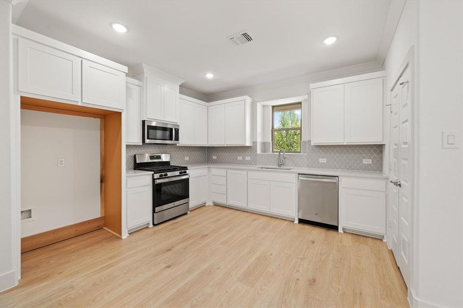 Kitchen featuring sink, stainless steel appliances, light hardwood / wood-style floors, and white cabinets