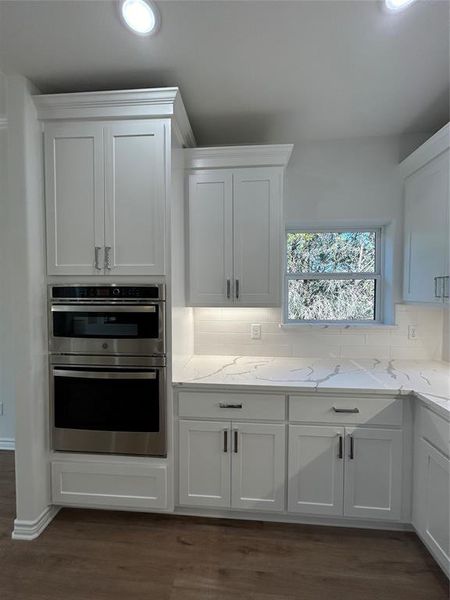 Kitchen featuring double oven, white cabinetry, and backsplash