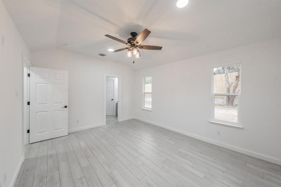 Empty room featuring lofted ceiling, ceiling fan, light hardwood / wood-style flooring, and plenty of natural light