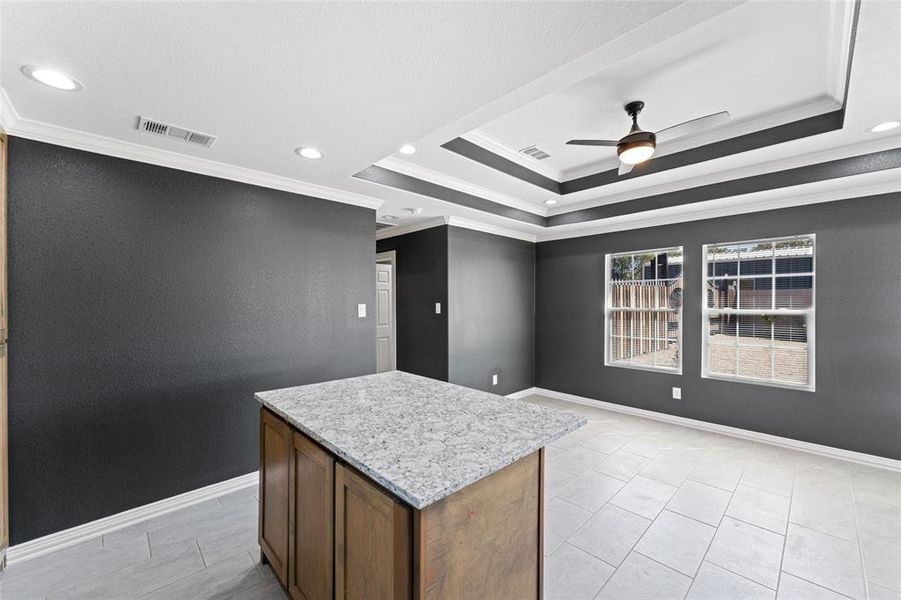 Kitchen featuring a kitchen island, light stone countertops, crown molding, and ceiling fan