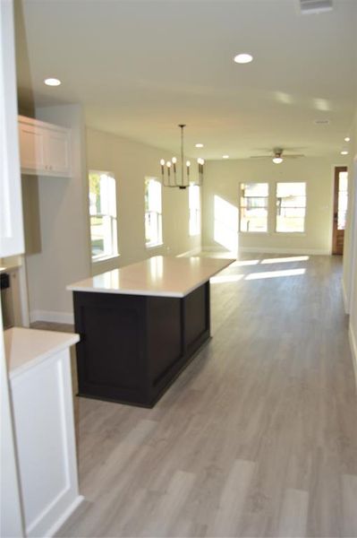 Kitchen featuring white cabinets, a center island, light LVP flooring, and a healthy amount of sunlight