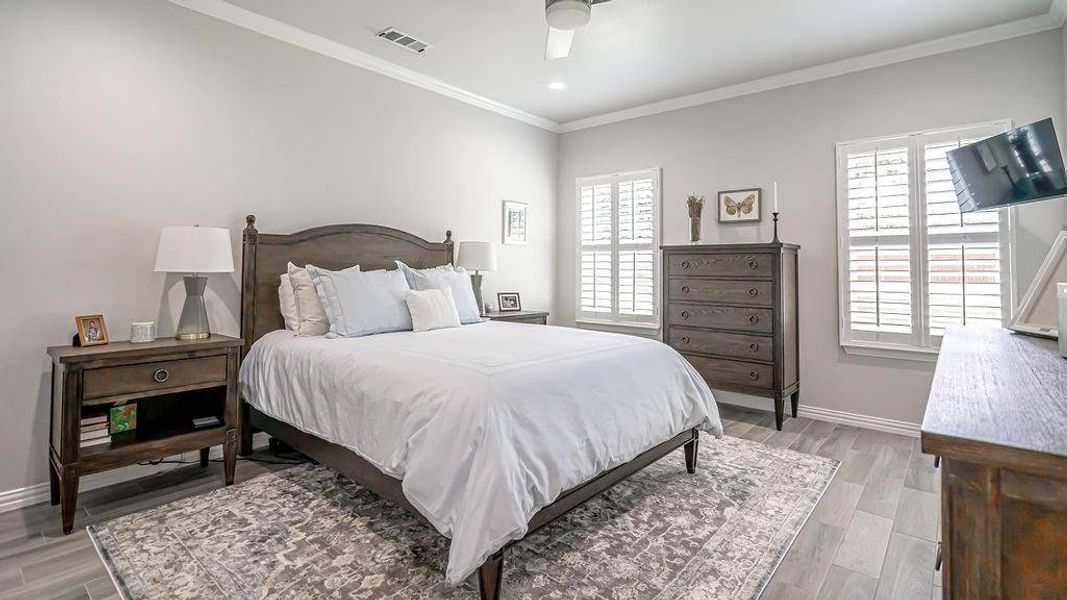 Bedroom with light hardwood / wood-style flooring, ceiling fan, multiple windows, and ornamental molding