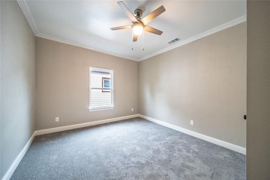 Carpeted empty room featuring ceiling fan and ornamental molding