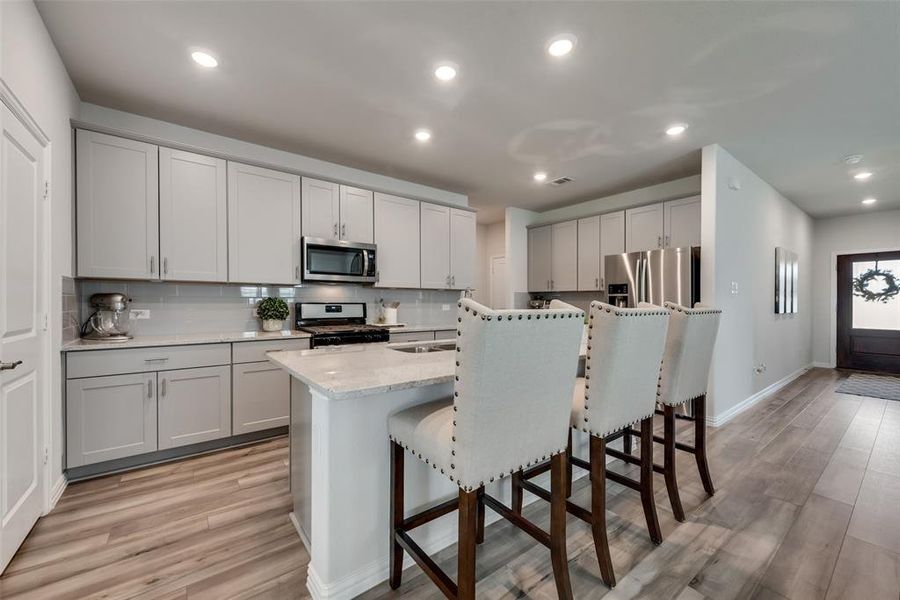 Kitchen with a kitchen breakfast bar, light hardwood / wood-style flooring, a center island with sink, backsplash, and appliances with stainless steel finishes