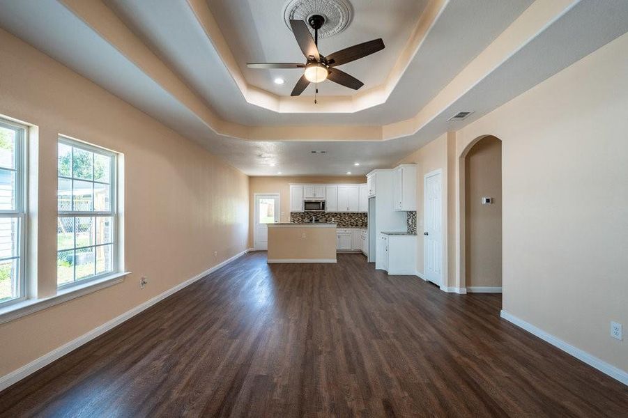 Living room with dark hardwood / wood-style floors, ceiling fan, and a raised ceiling.