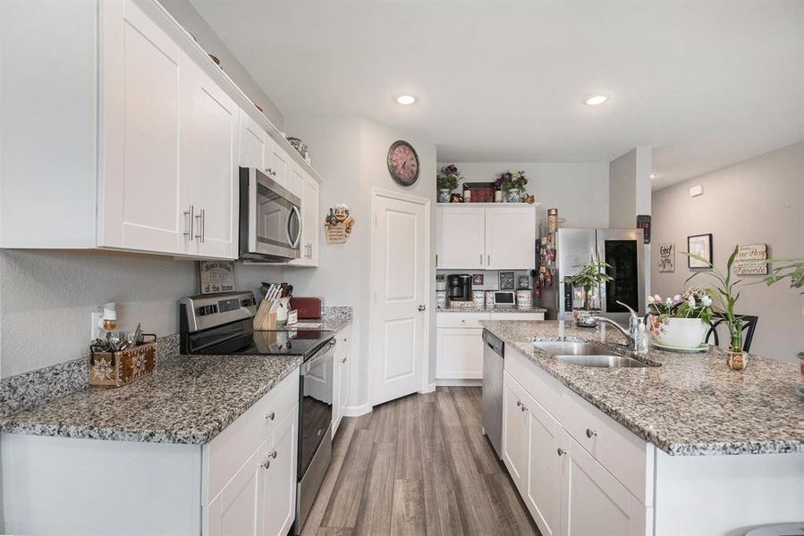 Kitchen featuring white cabinets, hardwood / wood-style floors, stainless steel appliances, sink, and a kitchen island with sink