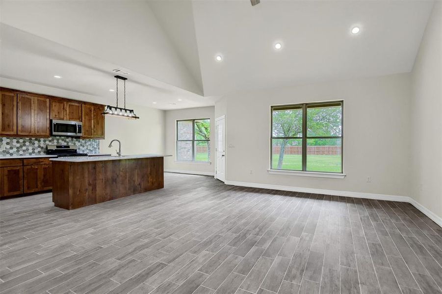 Kitchen with pendant lighting, high vaulted ceiling, a center island with sink, appliances with stainless steel finishes, and backsplash