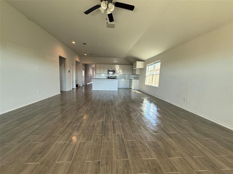 Unfurnished living room with dark wood-type flooring, ceiling fan, and lofted ceiling