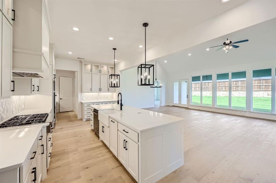 Kitchen featuring a kitchen island with sink, light wood-type flooring, tasteful backsplash, and white cabinets