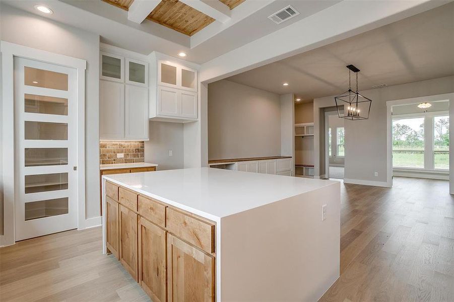 Kitchen with a center island, light hardwood / wood-style flooring, beam ceiling, decorative light fixtures, and tasteful backsplash