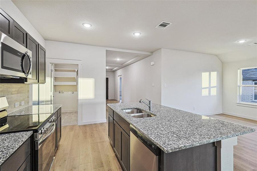 Kitchen featuring an island with sink, sink, tasteful backsplash, stainless steel appliances, and light wood-type flooring