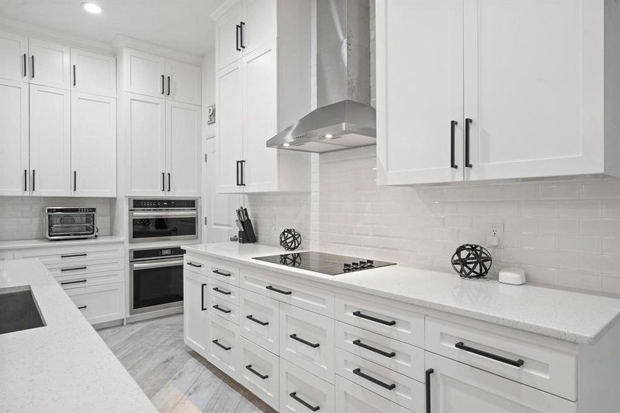 Kitchen featuring light hardwood / wood-style floors, white cabinetry, tasteful backsplash, wall chimney exhaust hood, and light stone countertops