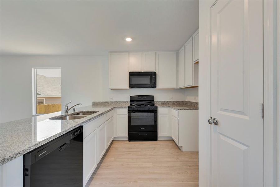 Kitchen with black appliances, sink, light hardwood / wood-style floors, light stone countertops, and white cabinetry