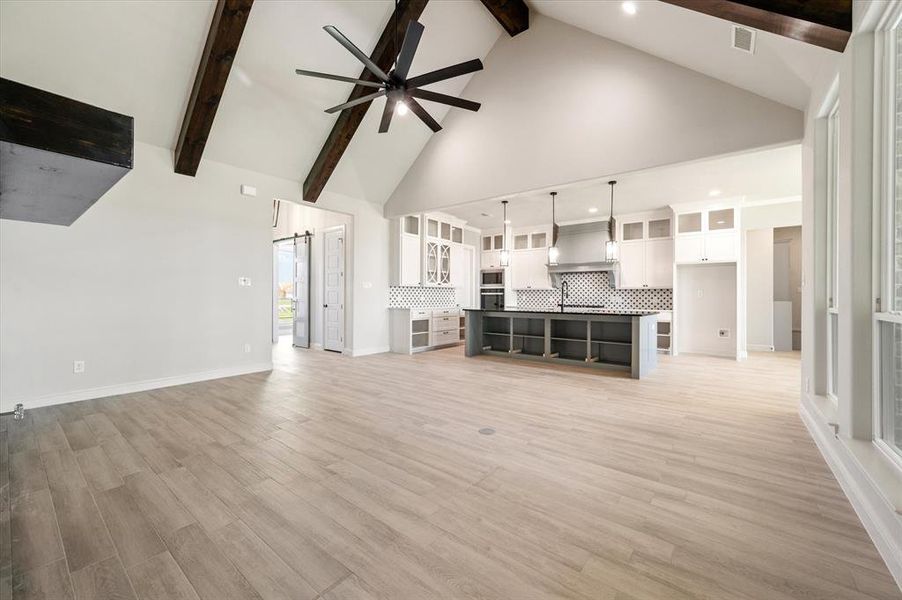 Unfurnished living room featuring light hardwood / wood-style flooring, beam ceiling, ceiling fan, and high vaulted ceiling