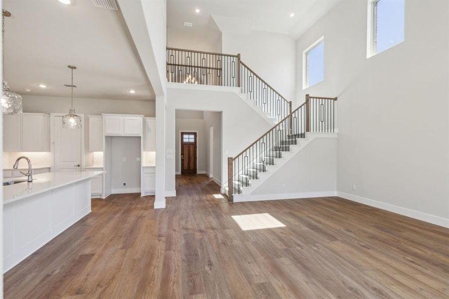 Unfurnished living room featuring a towering ceiling, sink, and light wood-type flooring