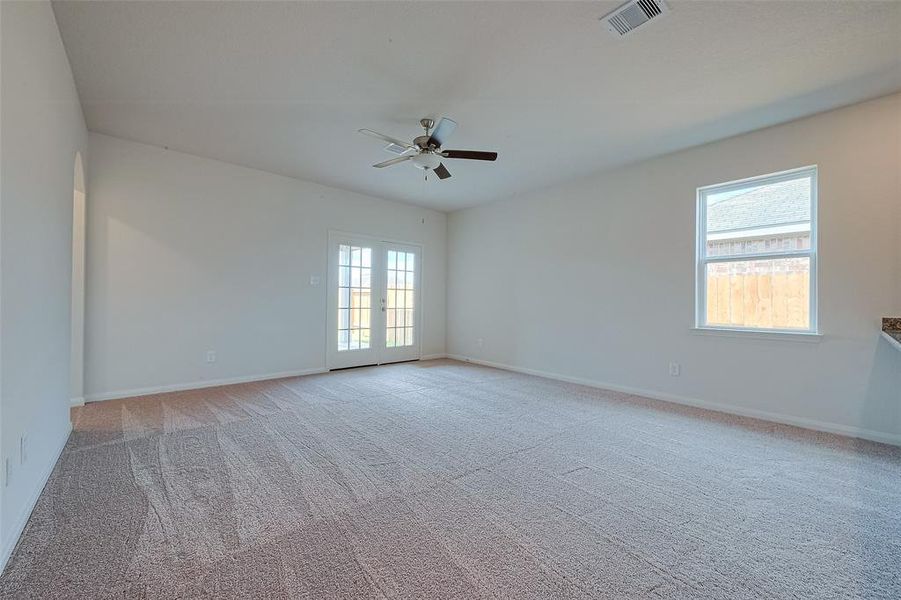 Empty room with carpet, ceiling fan, French doors leading outside, and a large window with a view of a wooden fence.