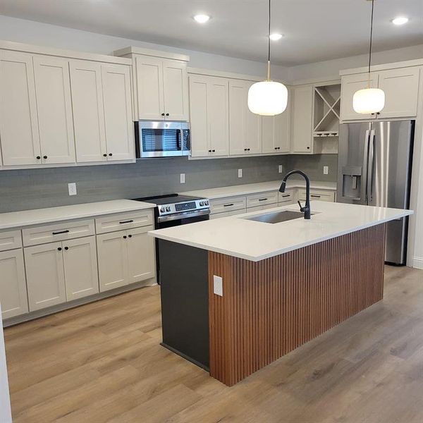 Kitchen featuring light hardwood / wood-style floors, decorative light fixtures, backsplash, sink, and appliances with stainless steel finishes