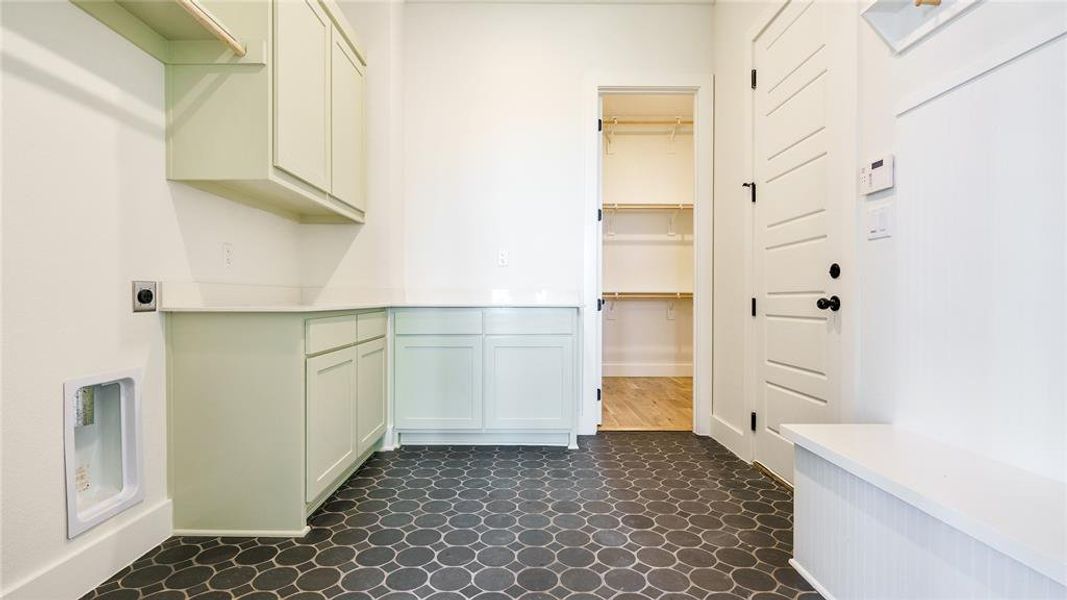 Washroom featuring electric dryer hookup, cabinets, and dark tile flooring