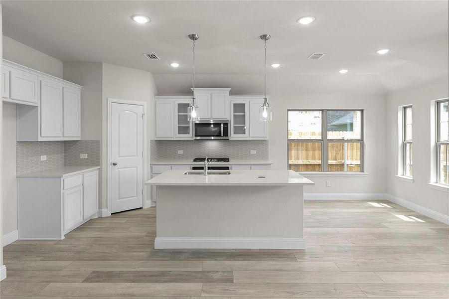 Kitchen with light hardwood / wood-style floors, backsplash, hanging light fixtures, a center island with sink, and white cabinets