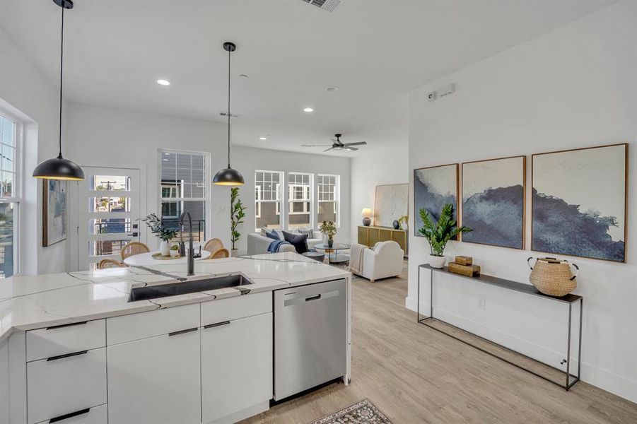 Kitchen featuring light wood-type flooring, sink, white cabinetry, decorative light fixtures, and stainless steel dishwasher