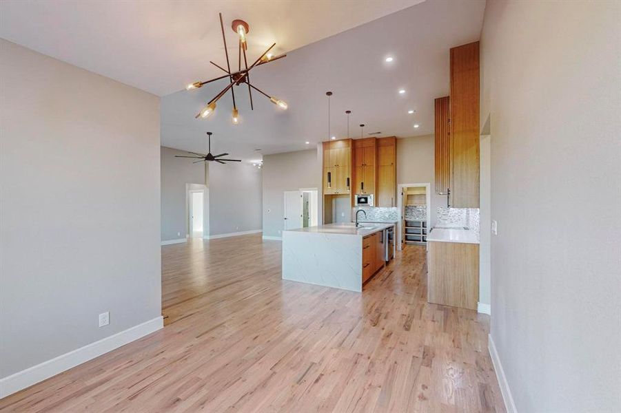 Kitchen with tasteful backsplash, sink, decorative light fixtures, light hardwood / wood-style flooring, and a center island with sink