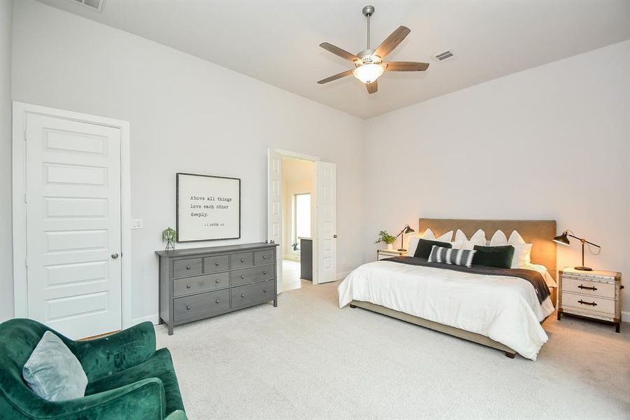 Well-lit primary bedroom featuring neutral walls, newly carpeted flooring, a ceiling fan, and large windows with a view of greenery outside. Also, includes a cozy sitting area for relaxation.