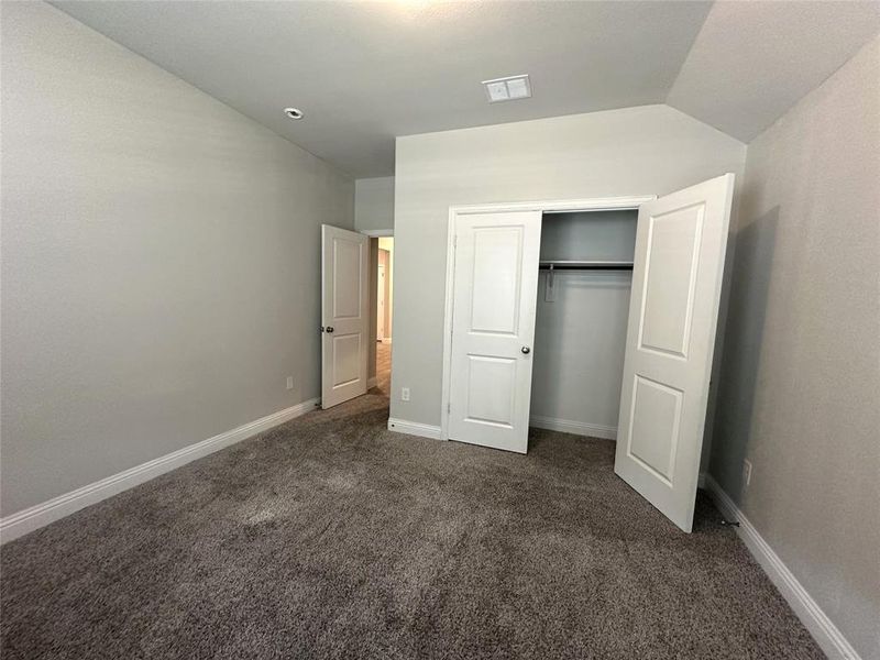 Unfurnished bedroom with a closet, vaulted ceiling, and dark colored carpet