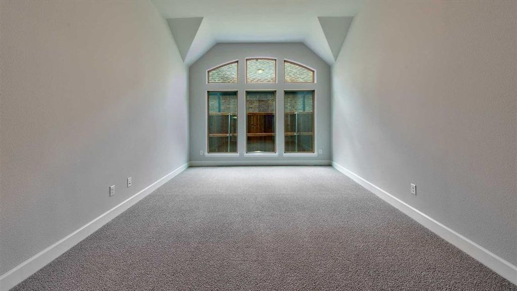 Carpeted spare room featuring vaulted ceiling