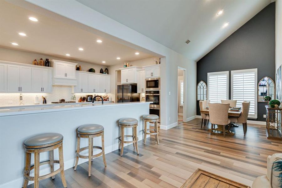 Kitchen with hardwood floors, kitchen peninsula, tasteful backsplash, stainless appliances and white cabinetry.  Dining Room and entrance to Laundry room.