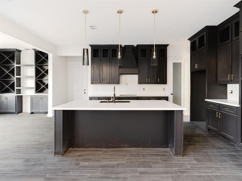 Kitchen with an island with sink, dark hardwood / wood-style flooring, decorative light fixtures, and custom range hood