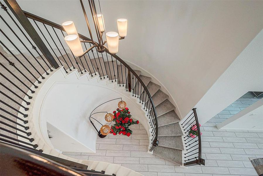 This image showcases a grand, curved staircase with a modern chandelier, wrought-iron balusters, and elegant tile flooring, enhancing the sophisticated ambiance of the entryway.