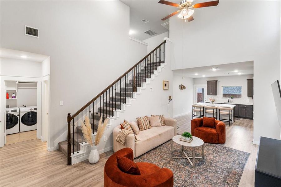 Living room with a towering ceiling, ceiling fan, separate washer and dryer, and light hardwood / wood-style floors