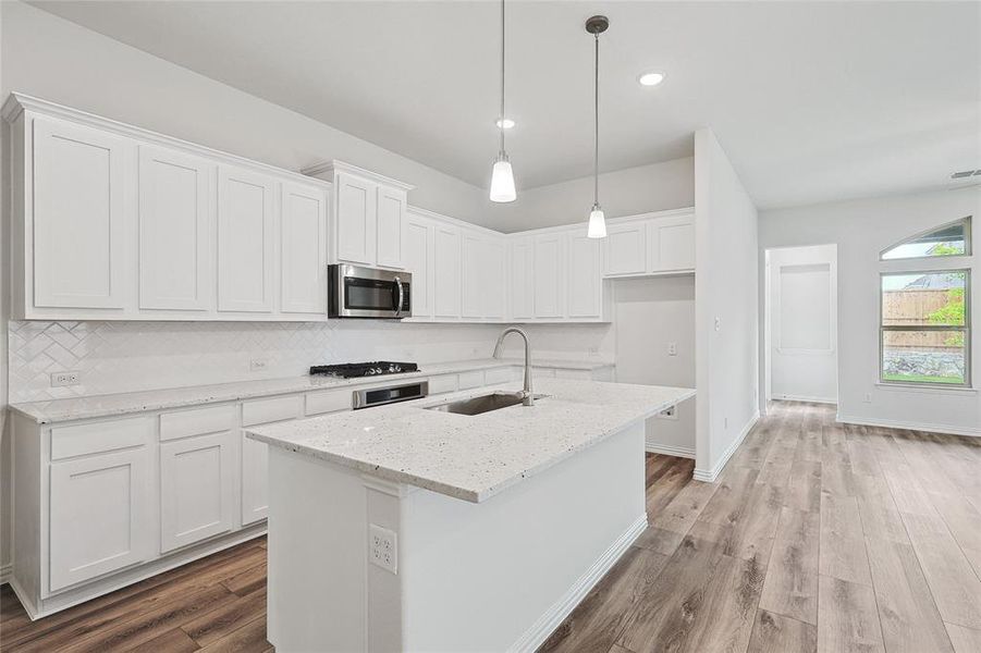 Kitchen featuring light hardwood / wood-style floors, sink, white cabinetry, and an island with sink