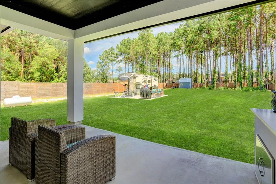 RELAX OR ENTERTAIN IN THIS EXPANSIVE BACKYARD, FEATURING A COVERED PATIO AREA PERFECT FOR DINING AL FRESCO, SURROUNDED BY LUSH GRASS AND A PRIVACY FENCE WITH A SERENE BACKDROP OF TALL PINES, OFFERING AN IDEAL SETTING FOR PRIVATE GATHERINGS AND TRANQUIL AFTERNOONS.