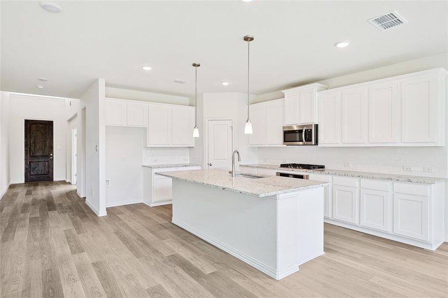 Kitchen with light wood-type flooring, white cabinetry, light stone countertops, sink, and a center island with sink