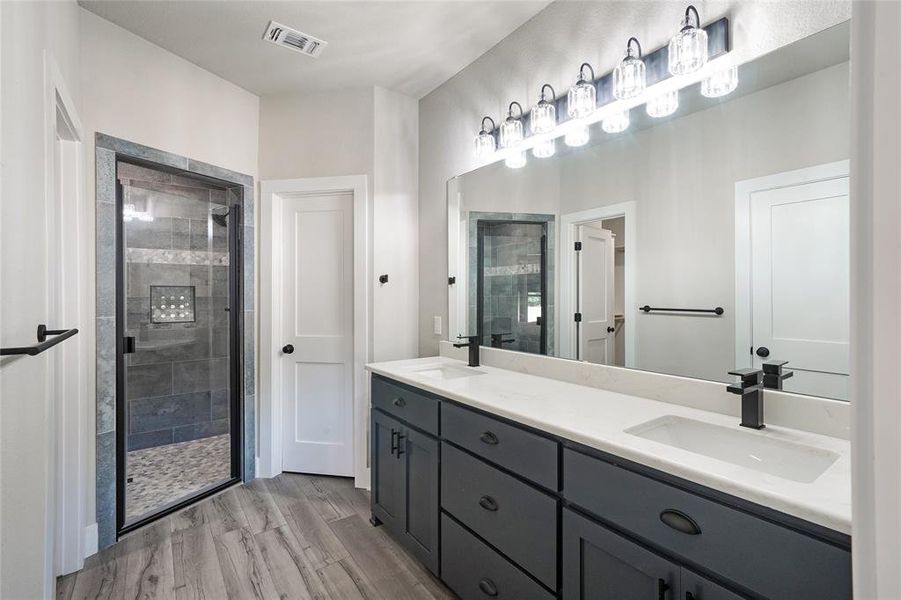 Primary Bathroom featuring a shower with shower door, hardwood / wood-style flooring, and vanity