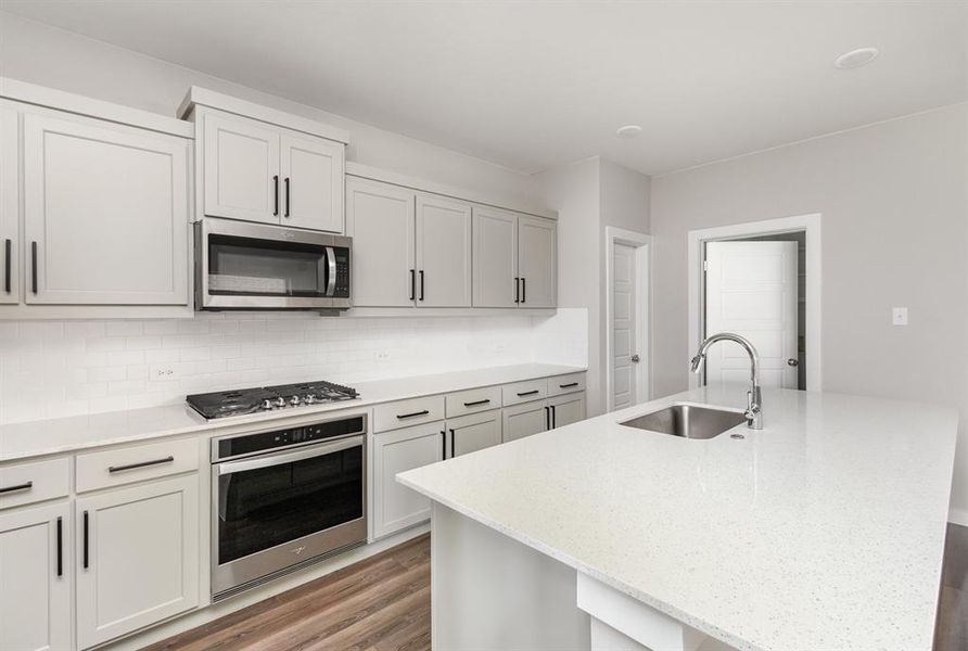 Kitchen featuring backsplash, appliances with stainless steel finishes, sink, hardwood / wood-style flooring, and a center island with sink