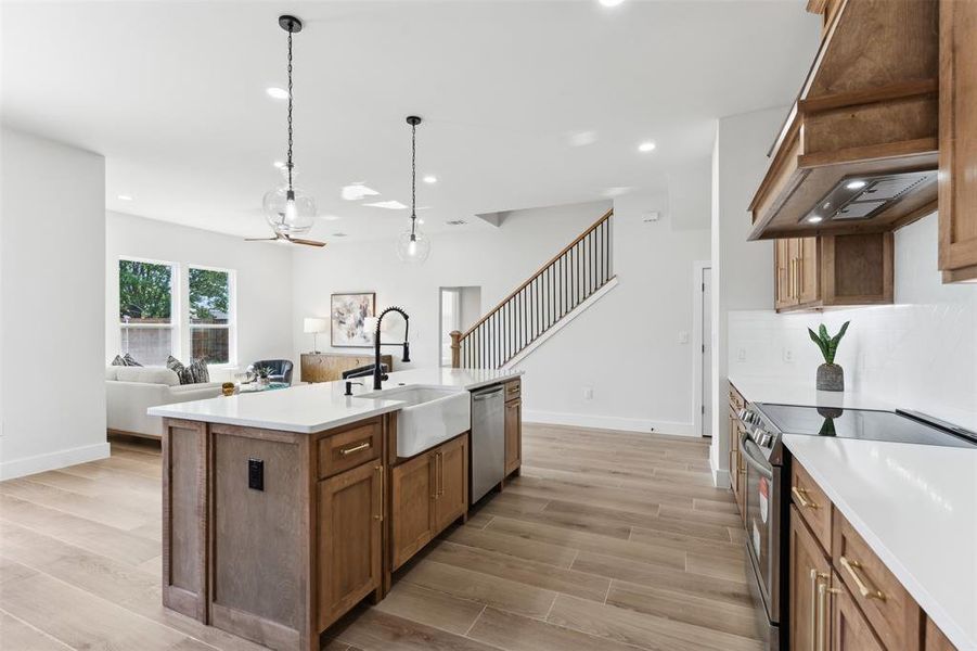 Kitchen with appliances with stainless steel finishes, custom range hood, an island with sink, and light hardwood / wood-style flooring