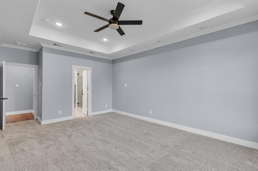 Unfurnished bedroom featuring ornamental molding, a tray ceiling, connected bathroom, carpet floors, and ceiling fan