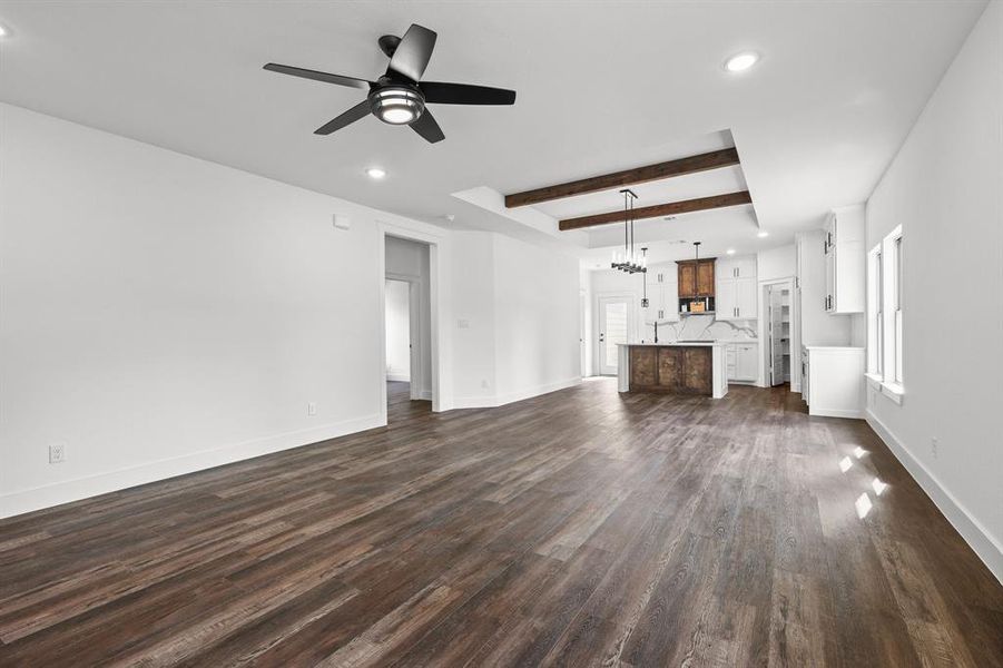 Unfurnished living room featuring ceiling fan with notable chandelier, beam ceiling, and dark hardwood / wood-style flooring