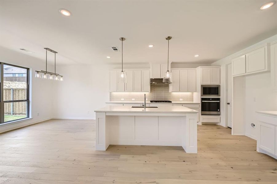 Kitchen featuring hanging light fixtures, decorative backsplash, a center island with sink, light hardwood / wood-style floors, and appliances with stainless steel finishes