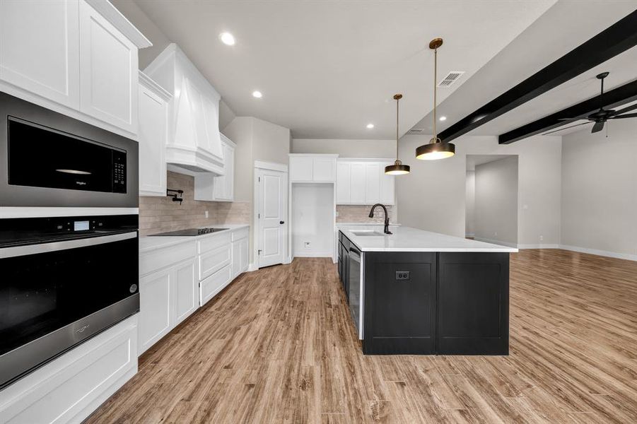 Kitchen with a kitchen island with sink, tasteful backsplash, light wood-type flooring, and pendant lighting