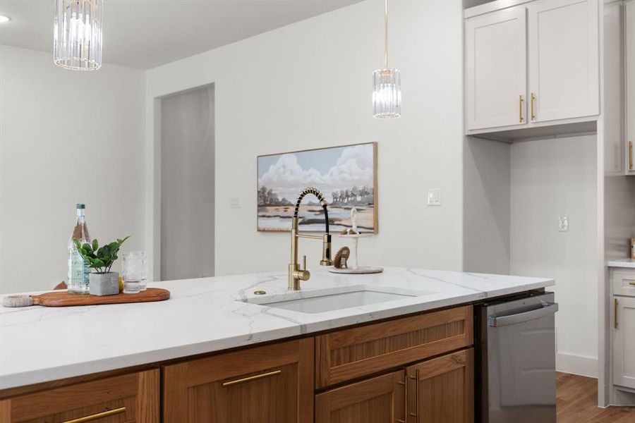 Kitchen with light stone counters, pendant lighting, sink, stainless steel dishwasher, and white cabinetry