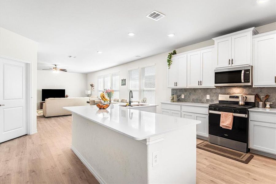 Kitchen featuring white cabinets, a center island with sink, appliances with stainless steel finishes, and light hardwood / wood-style flooring