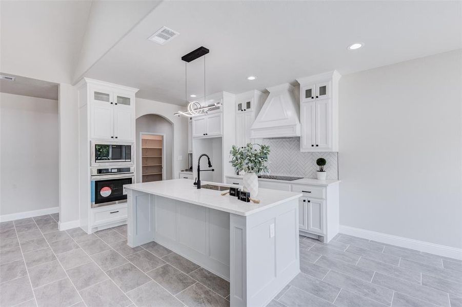 Kitchen with custom cabinets, gorgeous hood, appliances with stainless steel finishes, and sink